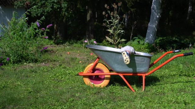 Little boy brother and his blond cute sister climbing into garden wheelbarrow.