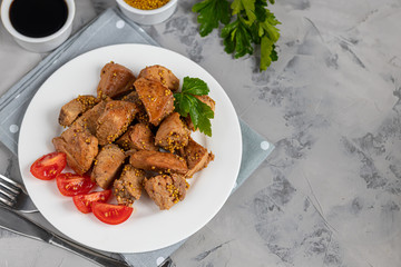 Fried and stewed chicken breast in soy-honey sauce. In the background mustard seeds, a box of vegetables for salad. On a plate are slices of tomato and razmarin. On a gray background.