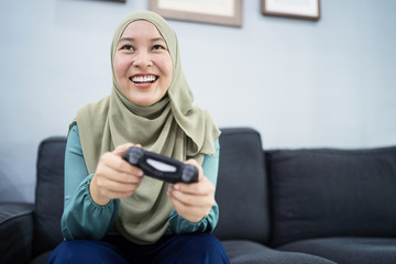 Fototapeta na wymiar Beautiful muslim woman playing console games at her couch.