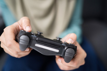 Beautiful muslim woman playing console games at her couch.