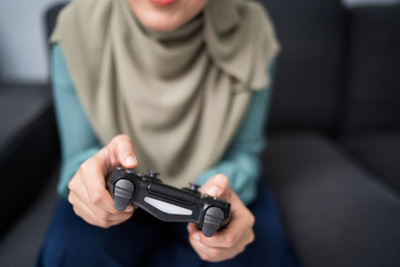 Beautiful muslim woman playing console games at her couch.