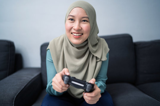 Beautiful muslim woman playing console games at her couch.