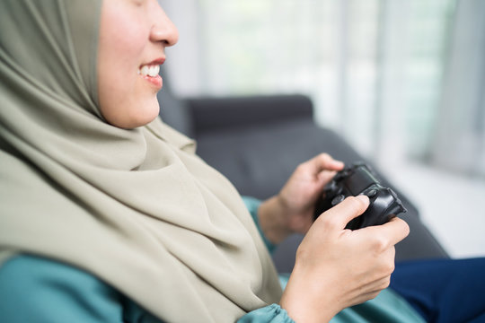 Beautiful muslim woman playing console games at her couch.