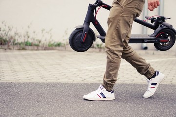 Young man with modern electric scooter on blurry city street background.