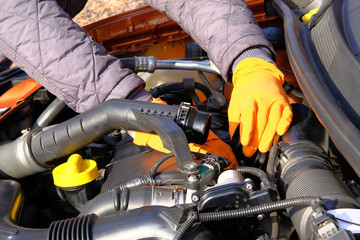 Automobile maintenance concept. Hands of driver in orange rubber gloves checks car, open hood. Cars...