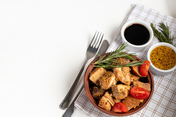 Fried and stewed chicken breast in soy-honey sauce. In the background mustard seeds, a box of vegetables for salad. On a plate are slices of tomato and razmarin. On white background.