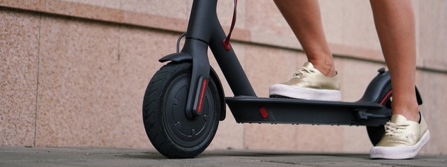 Young woman with modern electric scooter on blurry city street background.