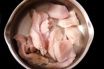 Raw chopped pieces of chicken lie in water in a pan, will be boiled, top view.