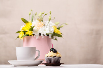 Cup of cocoa with marshmallows, a cupcake, a bouquet of flowers and a soft blanket in the background. Pleasant awakening