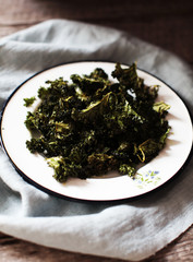 bunch of kale chips on a white plate on wooden table