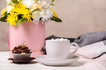 Cup of cocoa with marshmallows, a cupcake, a bouquet of flowers and a soft blanket in the background. Pleasant awakening