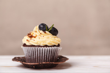 Delicious cupcake with whipped cream on background of beige wall. Concept of advertising confectionery products
