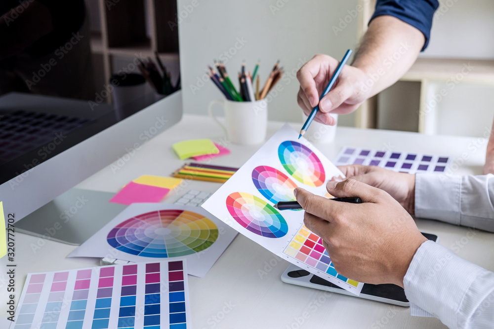 Poster Two colleague creative graphic designer working on color selection and color swatches, drawing on graphics tablet at workplace with work tools and accessories