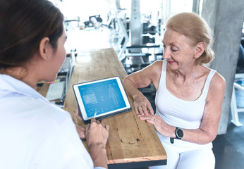 Doctor with senior woman in rehabilitation center check health care and showing data something on Tablet.
