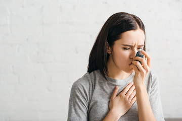 Sick woman using asthmatic inhaler at home - obrazy, fototapety, plakaty