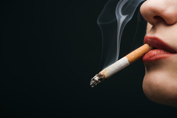 Cropped view of woman smoking cigarette isolated on black