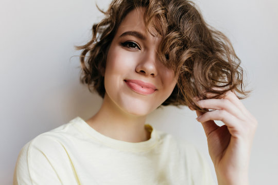 Close-up portrait of happy young woman with trendy makeup playing with short hair. Indoor photo of enchanting curly girl isolated on white background.