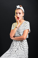 Young surprised girl with pin-up make-up and hairstyle posing in studio.