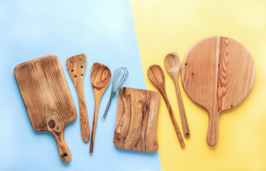 Kitchen utensils, food preparation cooking accessorises, chopping boards, wooden spoons, whisk on blue and yellow table, top view, selective focus