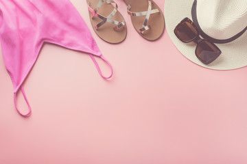Straw hat, sunglasses, fuchsia colored swimsuit and golden shoes on pink background, beach holiday concept. Top view, selective focus