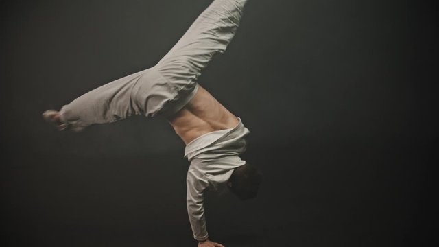 Young sportive man training his breakdancing tricks in the dark studio