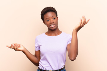 young pretty black womanshrugging with a dumb, crazy, confused, puzzled expression, feeling annoyed...