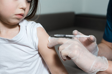 Man pediatrician performs a vaccination of a little scared girl whith syringe