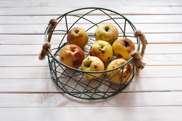 Ugly apples in metal basket on light wooden surface. Food waste.