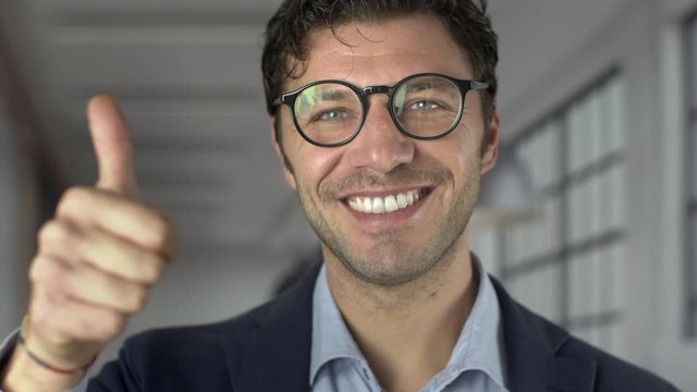 Portrait of happy successful businessman with black glasses giving a thumbs up for a success deal agreement. Confident handsome guy. Shot in 6k.