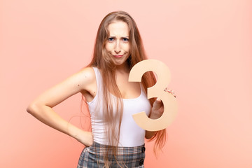 yound blonde woman angry, anger, disagreement, holding a number 3.