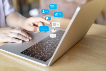 Person hands using social media marketing concept on laptop computer with notification icons of like, chat, message and comment above laptop screen.