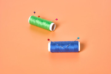 Spools with green and blue threads and needles on orange tailors desk in workshop. Close-up