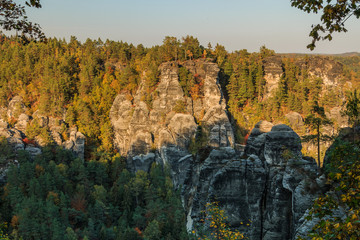 Evening sun in Saxon Switzerland. National park in the Elbe Sandstone Mountains for hiking and climbing in autumn mood. View of a rock formation with trees and a blue sky