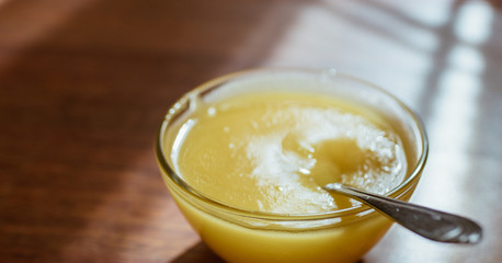 Round glass bowl with honey and spoon on a sunny wooden table