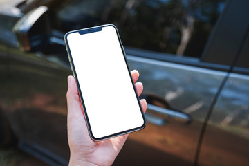 Mockup image of a woman holding and using mobile phone with blank screen with a car in background