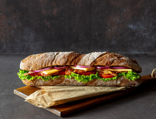 Ein Sandwich aus dunklem Brot mit Salat, Speck, Tomaten, Käse und Zwiebeln. Frühstück. Fastfood.