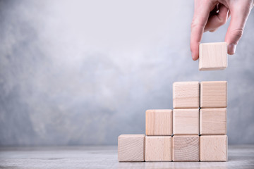 Hand arranging wood block stacking as step stair on wooden table. Business concept for growth...