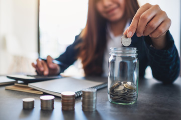 Closeup image of a businesswoman stacking and putting coins in a glass jar