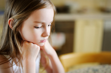 Bored little girl sitting by the table.