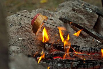 A piece of meat and bread is fried on fire. Bread on skewers near bonfire. Cooking on a hike.