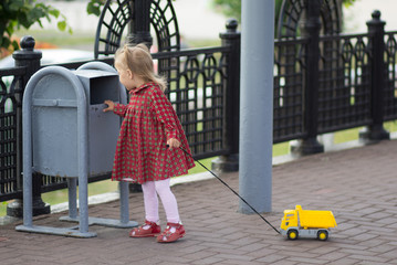 Caucasian child of two years old walking with toy car looking at garbage container