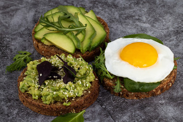Avocado sandwich on dark rye bread with spinach and fried egg on a dark background
