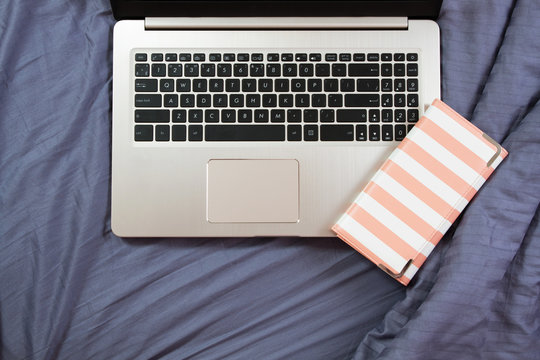flat lay image of workplace background, laptop and clatch on bed close up