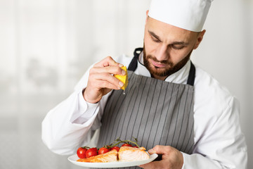 Male Chef Squeezing Lemon Plating Roasted Salmon Steak In Kitchen