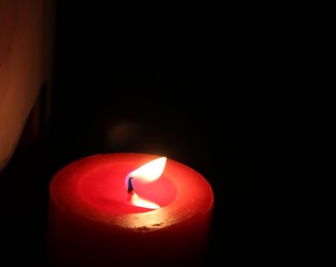 A red candle burns and lights up a dark background
