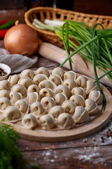 Russian national cuisine. Raw meat dumplings laid out on a cutting board with vegetables, herbs and specs on a flour-sprinkled wooden table.