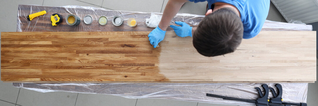Top view of handy man covering wooden desk with oil