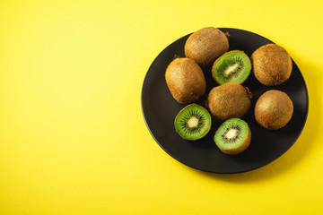 Kiwi fruits half sliced in black plate on vibrant plain yellow background, copy space, angle view