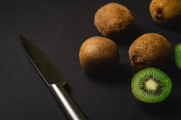 Kiwi fruits half sliced with kitchen knife on dark black moody plain background, angle view