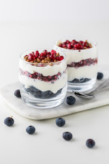 A close up of two pomegranate and blueberry parfaits layered with vanilla greek yogurt and granola.